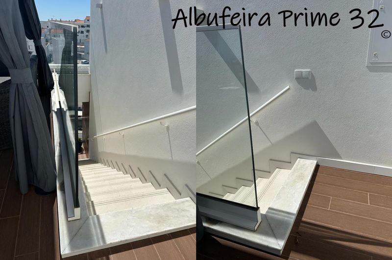 Stairs down from the roof terrace, with a glass safety panel along the open side and a handrail on the wall